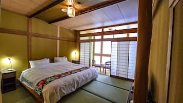 A traditional Japanese-style bedroom with tatami flooring, a large bed with white bedding, and sliding shoji doors.