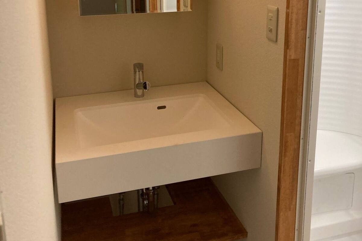A bathroom with a white sink, a mirror, and a wooden shelf below the sink.