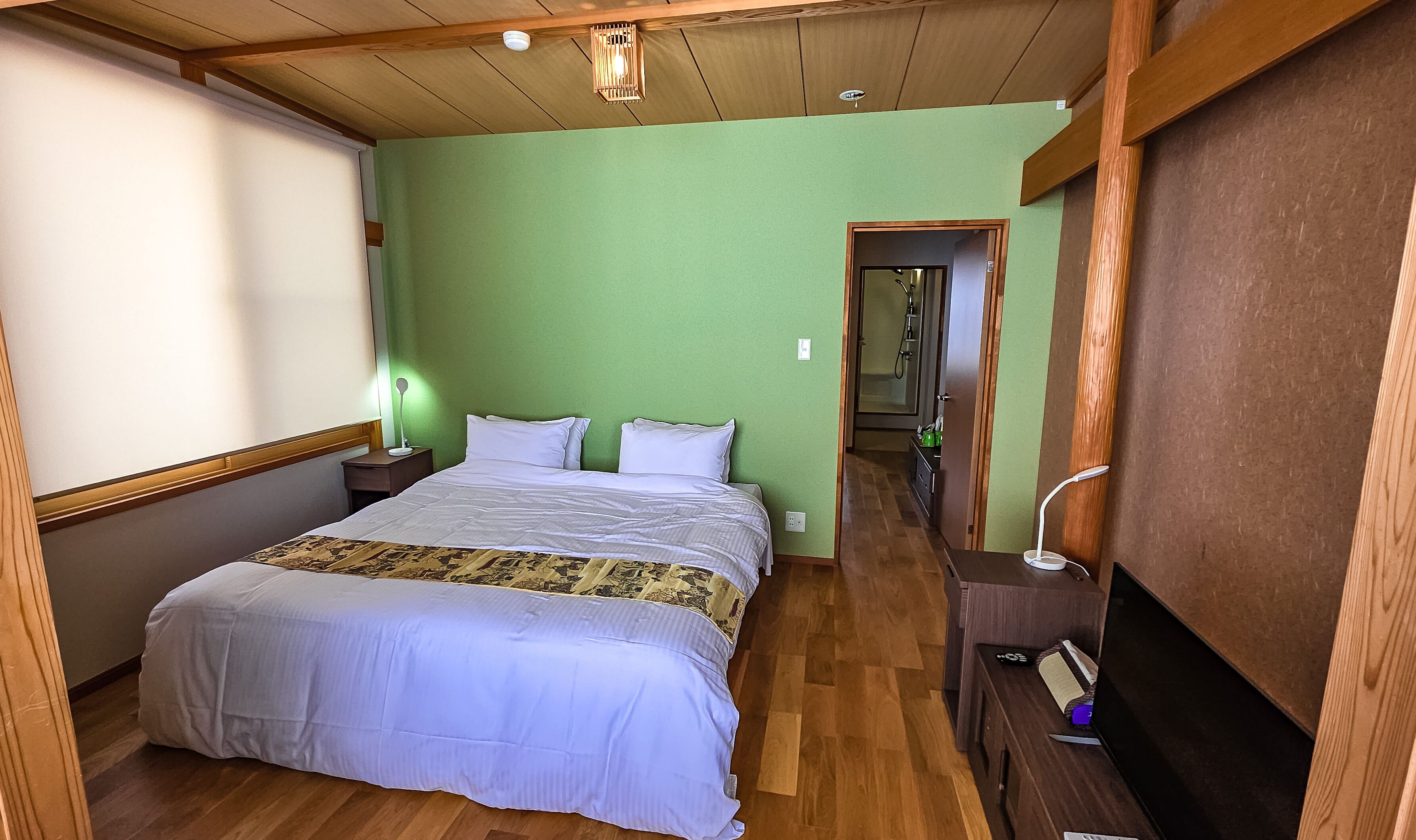 A bedroom with a bed, bedside tables, a nightstand, a mirror, and a wooden ceiling.