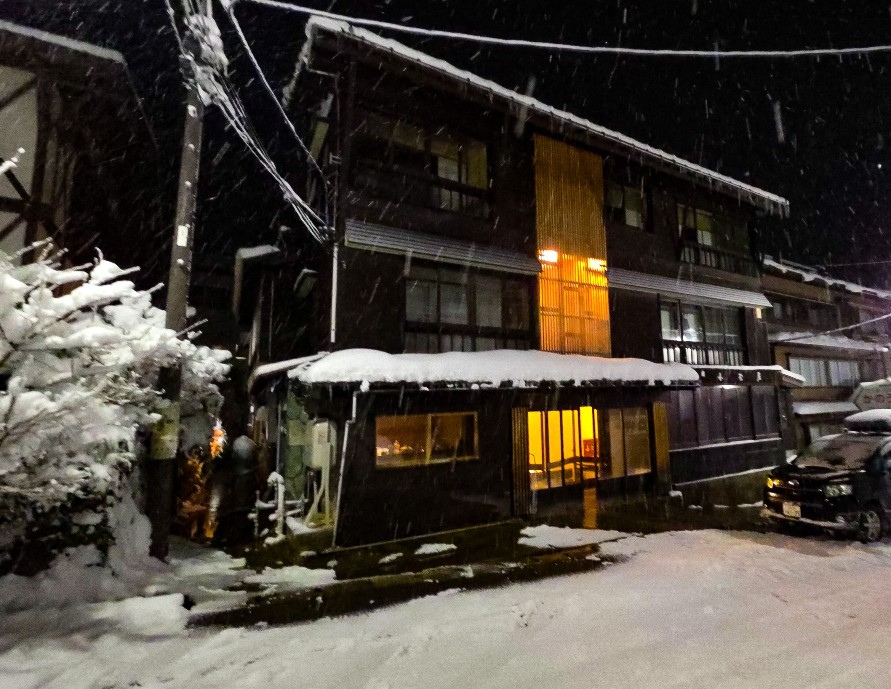A building with a snow-covered roof and a lit window, surrounded by snow.