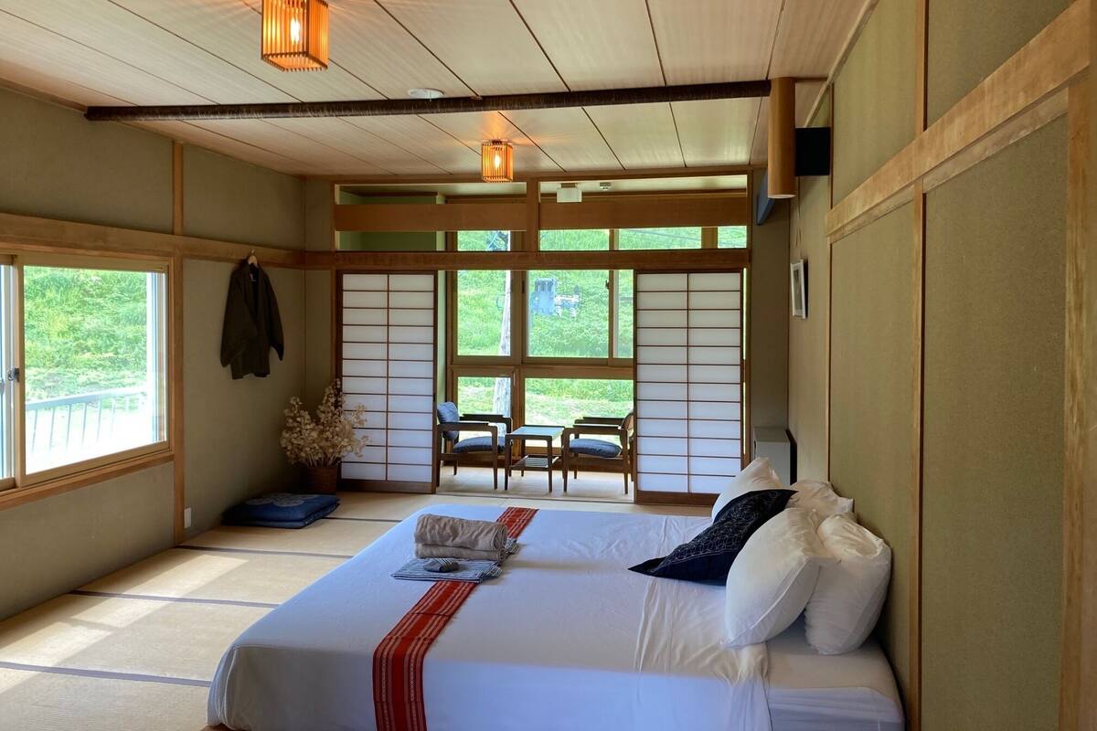 A traditional Japanese-style room with tatami flooring, a low bed with pillows, a small table, and chairs.