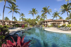 Ein Resort-Pool mit Palmen, Liegestühlen und einem Wasserfall.