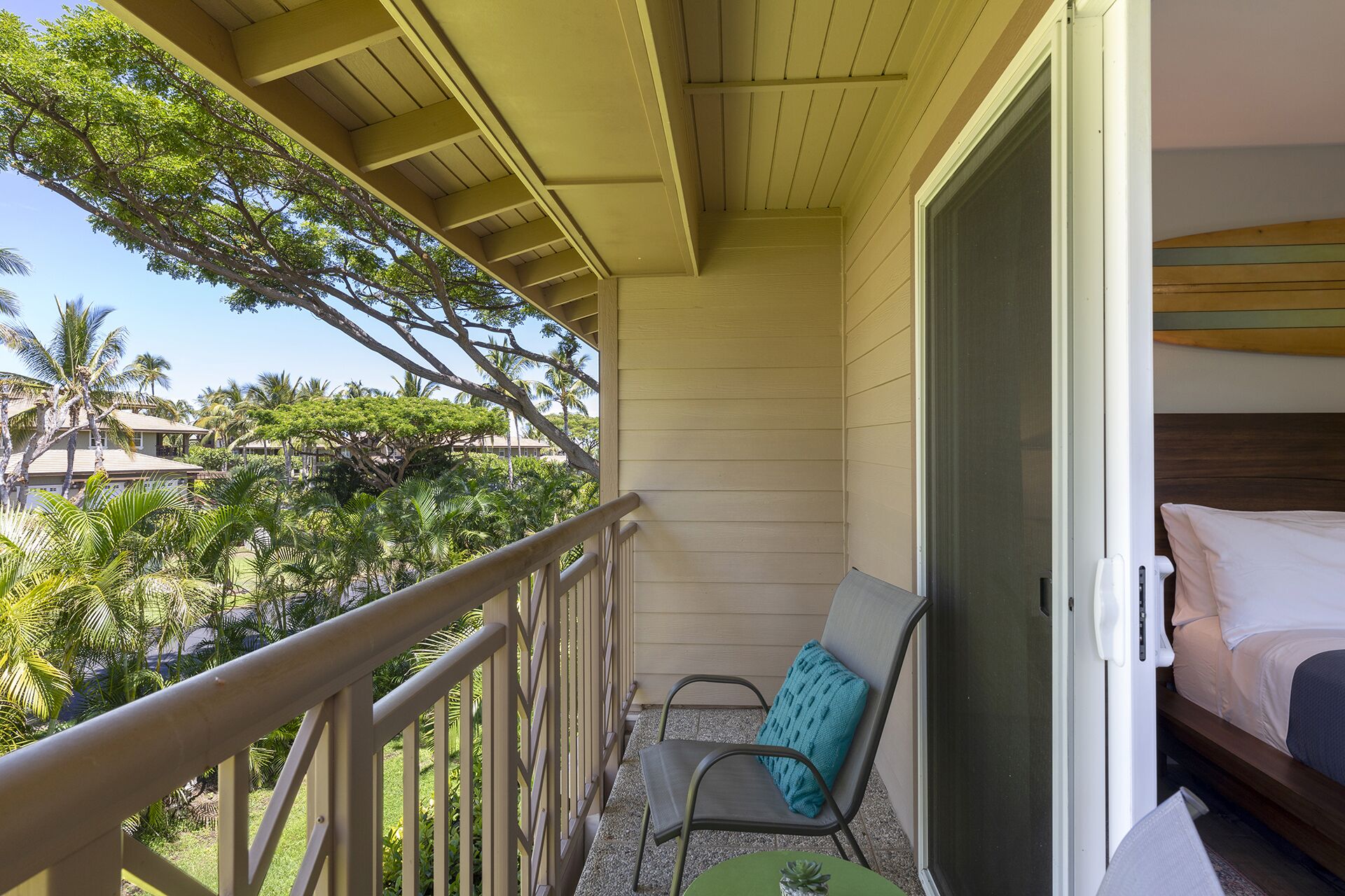 A balcony with a chair and a small table, overlooking a lush garden and other buildings.
