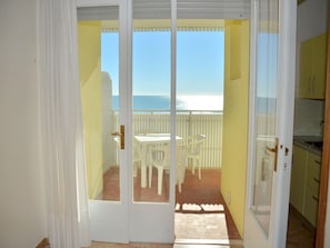 A sliding glass door leading to a balcony with a table and chairs, overlooking a beach.