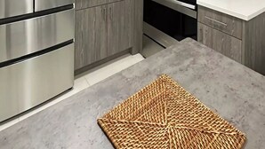 Moderni keittiö, jossa on valkoiset kaapit, ruostumattomasta teräksestä valmistetut kodinkoneet ja kudottu matto.