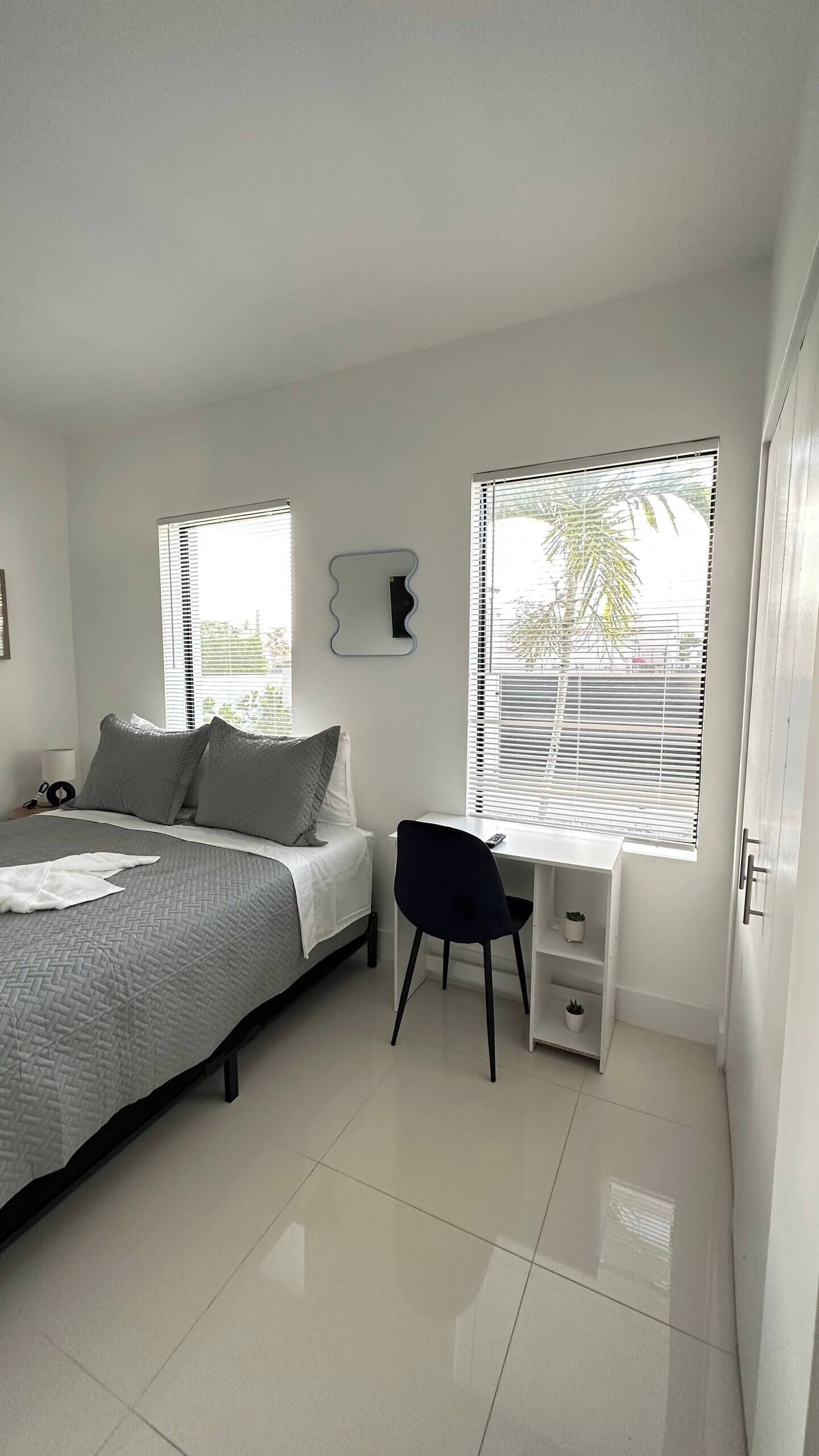 A bedroom with a bed, a desk, and two windows with blinds.