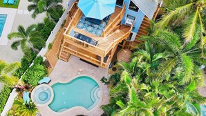 Una terrazza in legno a più livelli con arredi da esterno, una piscina e vegetazione tropicale rigogliosa.
