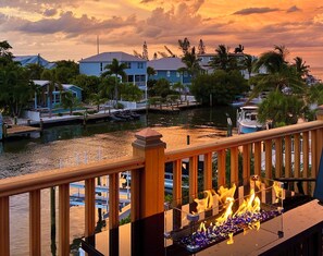 A waterfront view with a wooden deck, boats, and houses in the background. - Waterfront, Heated pool & spa, Elevator, Dock, Fire Pit, 4-min walk to beach (Holmes Beach)
