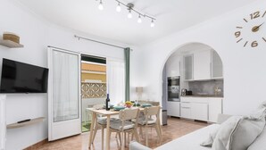 Un espace de vie moderne et compact comprenant un coin repas, une kitchenette et un téléviseur fixé au mur.