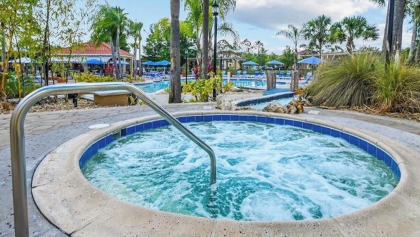 Ein Whirlpool mit einer Metallleiter, umgeben von Palmen und einem Poolbereich mit Liegestühlen.