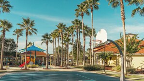 Ein Basketballplatz mit blauer Oberfläche, umgeben von Palmen und einem Spielplatz mit einer roten Rutsche.