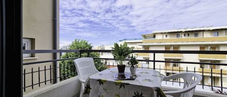 Un balcon avec une table et des chaises, un pot de fleurs et une vue sur les bâtiments en arrière-plan.