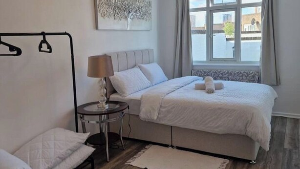 A bedroom with a bed, bedside table, lamp, and a view of the outside. - 1 Bed Flat Sleeps 2 with Free Parking & Patio (London)