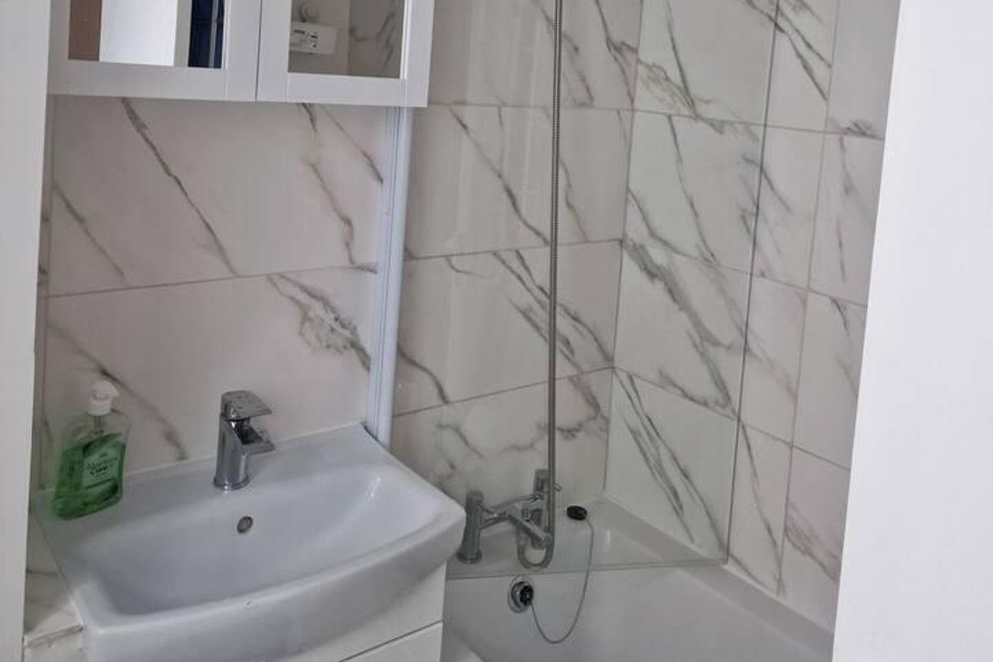 Ein Badezimmer mit einem weißen Waschbecken, einem Spiegelkorpus und einer Dusche mit Marmorfliesen.