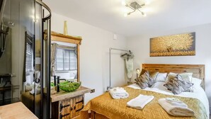 Ein Schlafzimmer mit einem Bett, einem Nachttisch, einem Spiegel, einem Fenster und einem Wandbild.