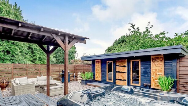 Ein Bereich mit Whirlpool, einer Holzterrasse, Gartenmöbeln und einem Gebäude mit Holztüren.