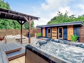A hot tub area with a wooden deck, outdoor furniture, and a building with wooden doors. - Luxury 2 bedroom Lodge in rural lincolnshire (Boston)