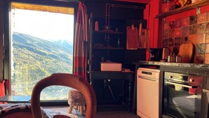 A kitchen with a view of mountains, a wooden chair, a small stool, a dishwasher, and a stove. - Chalet mountain and dog friendly, hot tub (Bourg-Saint-Maurice)