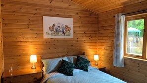 Et træhytte-værelse med en seng, to sengeborde med lamper, et vindue med gardiner og et billede af dyr på væggen.