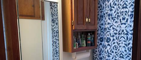 A bathroom with a vanity, a mirror with lights, a toilet, and patterned curtains.