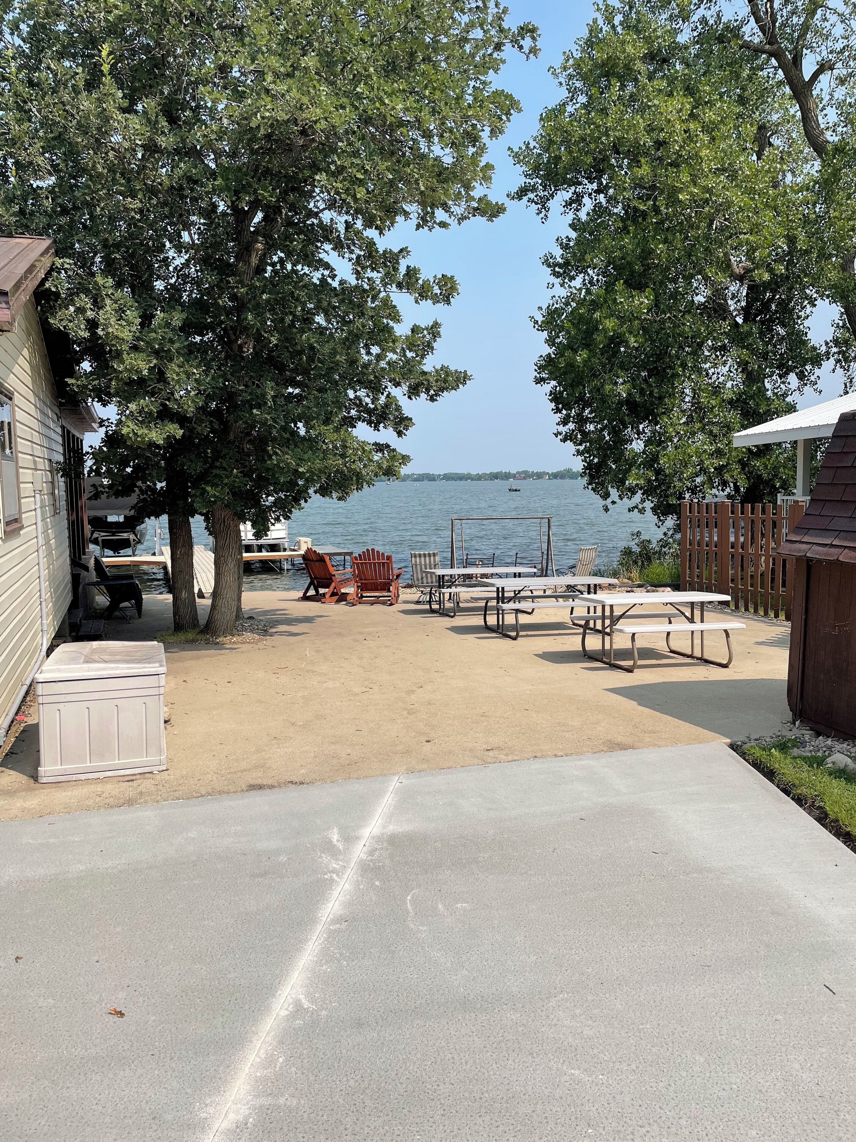 A waterfront patio with picnic tables and chairs, a small shed, and a wooden deck.