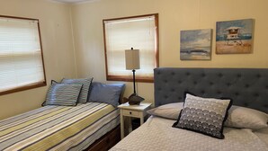 Un dormitorio con dos camas, una mesita de noche, una lámpara y dos cuadros en la pared.