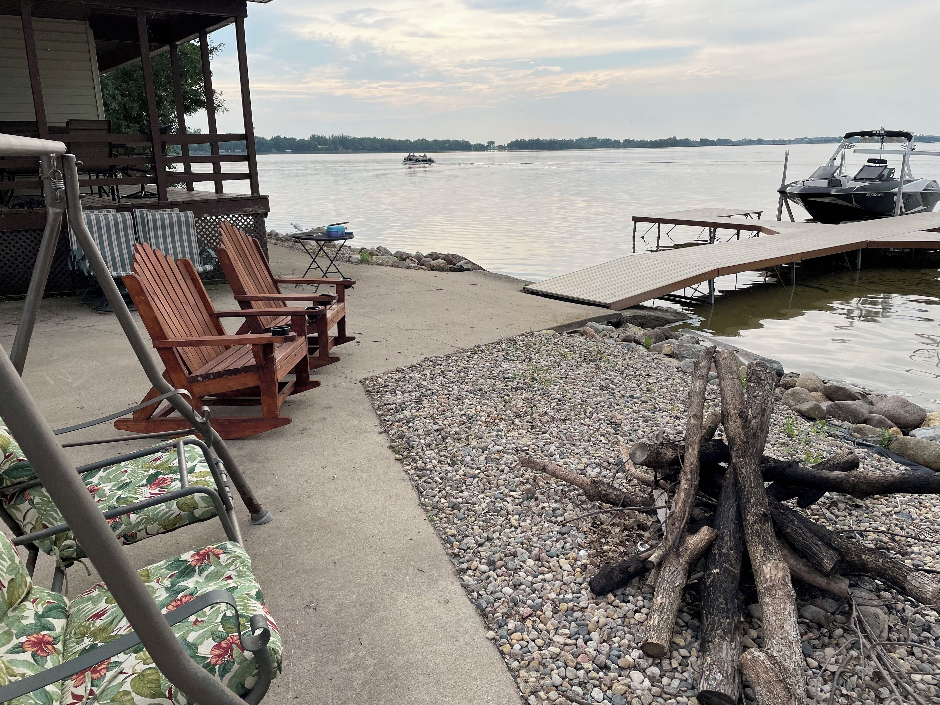 Terraza junto al lago con sillas de madera, una pequeña mesa y un embarcadero que se adentra en el agua.
