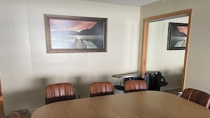 Un salón de conferencias con una mesa de madera, sillas de cuero, un espejo grande y un cuadro en la pared.
