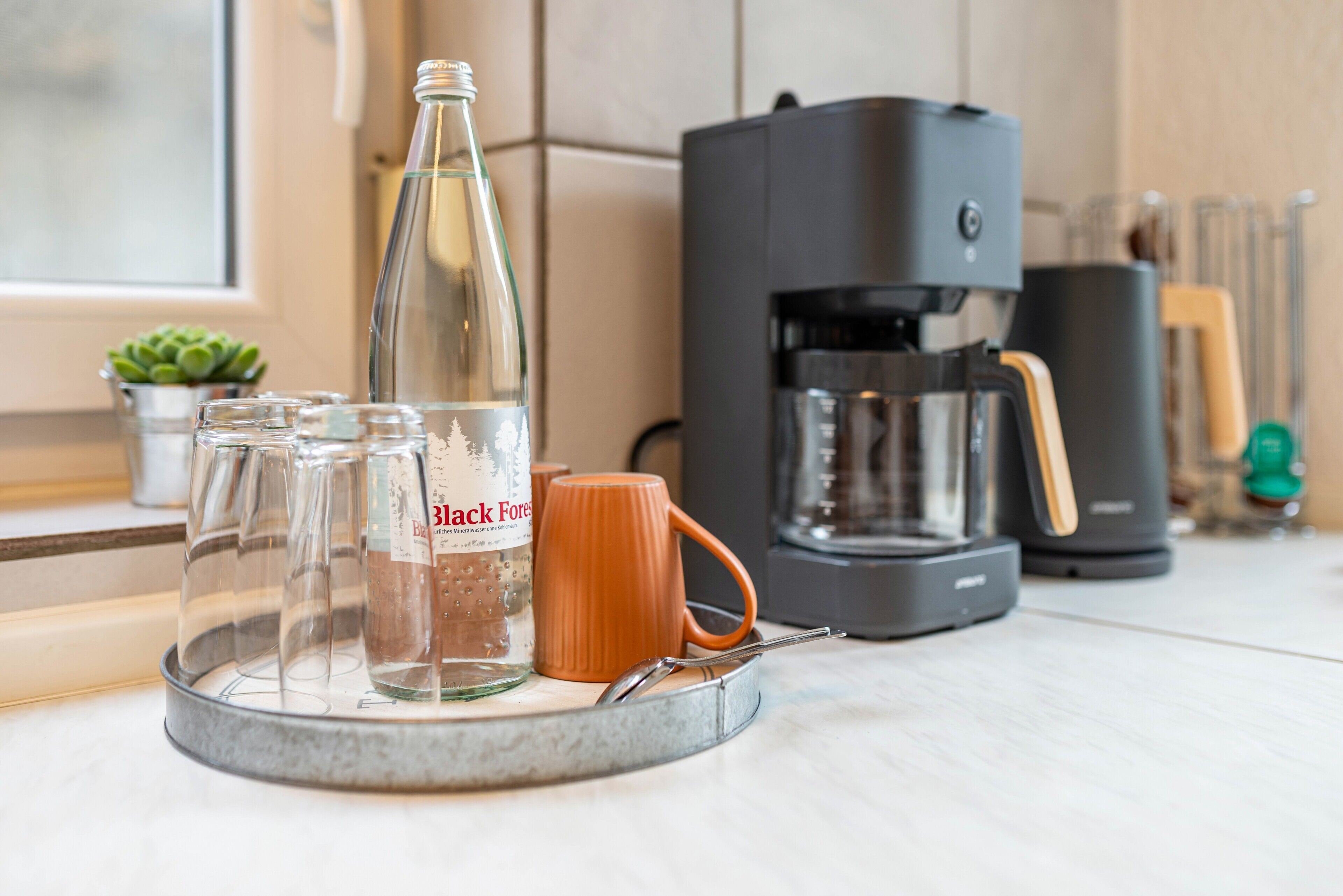 En køkkenbordplade med kaffemaskine, en glasflaske og en kop.