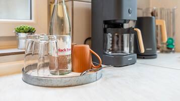 En køkkenbordplade med kaffemaskine, en glasflaske og en kop.