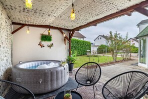 Ein überdachter Außenbereich mit Whirlpool, Stühlen und einer Pergola mit hängenden Lichtern.