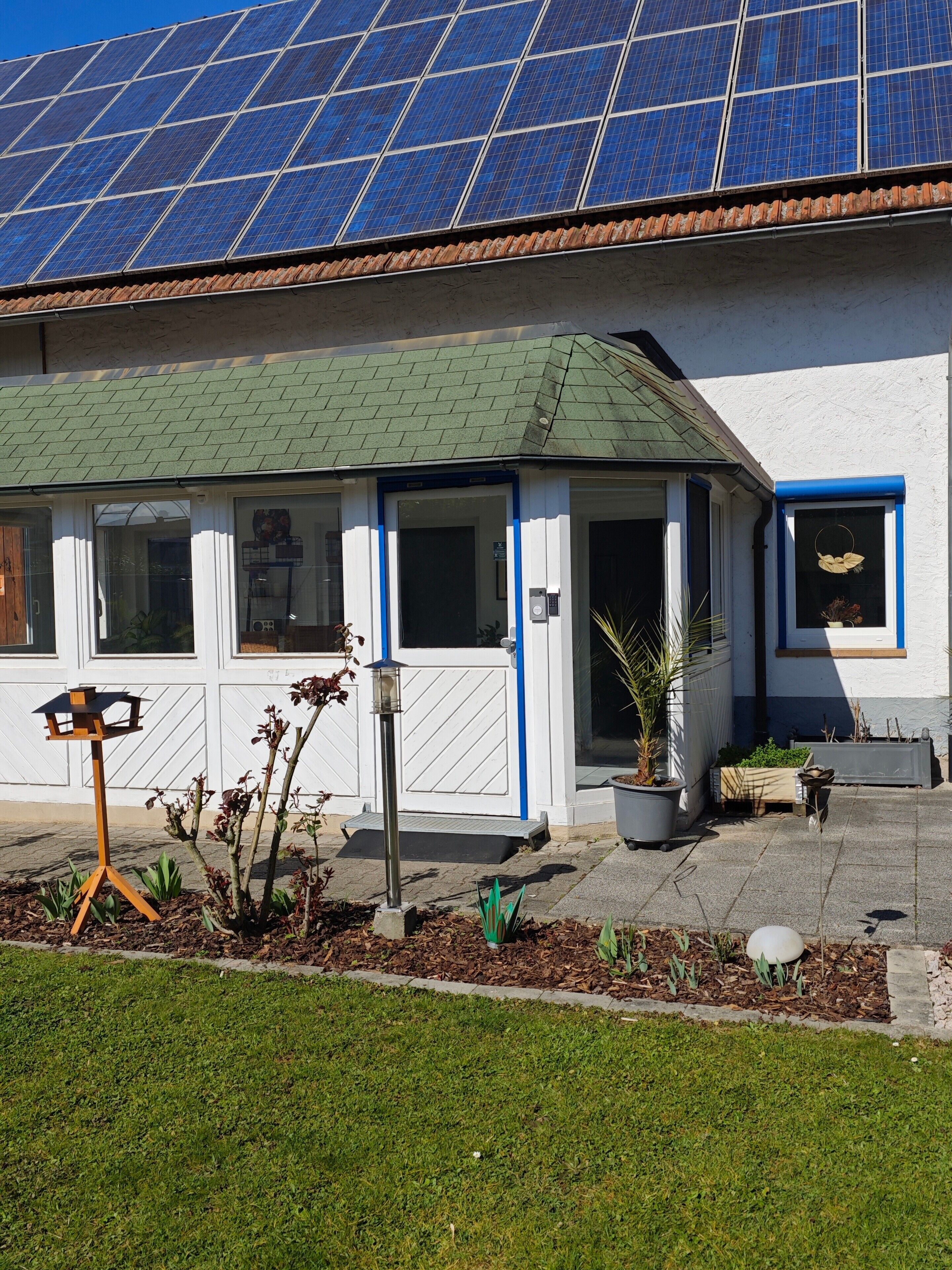 Un bâtiment doté d’un toit végétalisé, de panneaux solaires et d’un petit jardin avec des plantes en pot.