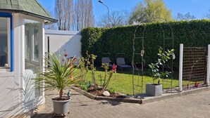 Una propiedad residencial con entrada pavimentada, jardín con plantas en macetas, seto y valla.