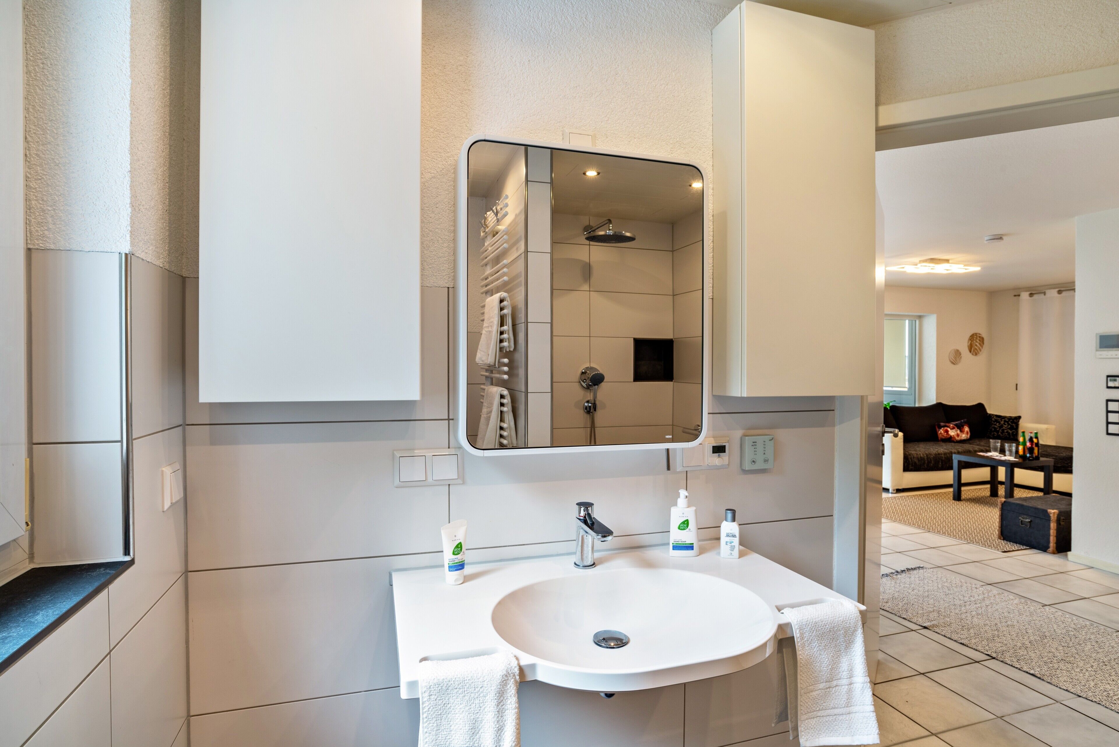 A modern bathroom with a large mirror, white sink, and a shower.