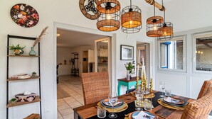 Un comedor con una mesa de madera dispuesta para cuatro, sillas de mimbre y un colgador de luz.