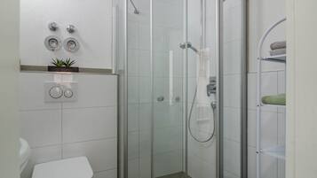 Ein modernes Badezimmer mit einer gläsernen Duschkabine, einer Toilette und einem Regal mit Handtüchern.