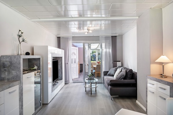 A modern living room with a sofa, coffee table, and a fireplace. There is a door leading to a balcony. - Holiday Home "Ihme" with Shared Garden & Wi-Fi (Sande)