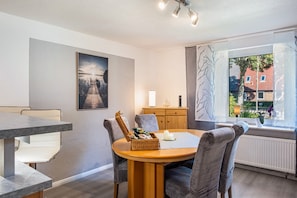 A dining area with a round table, grey upholstered chairs, a wicker basket, a white candle, and a painting on the wall. - Holiday Home "Ihme" with Shared Garden & Wi-Fi (Sande)