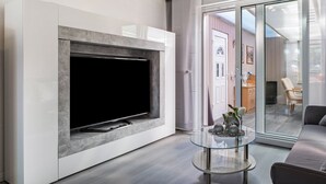 Una sala de estar moderna con un televisor de pantalla plana, una mesa de centro de vidrio y una puerta corrediza de vidrio que da a un comedor.
