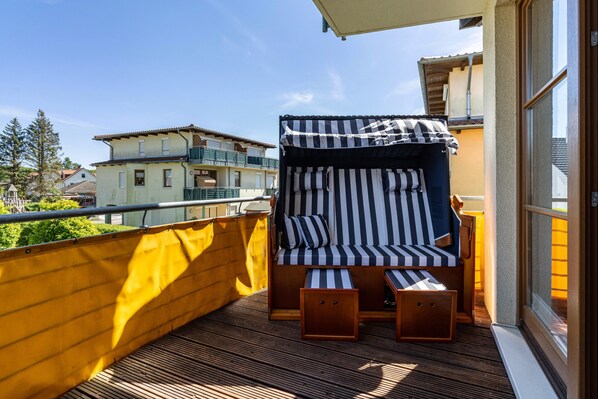 A balcony with a striped sofa, two wooden side tables, and a yellow safety barrier.