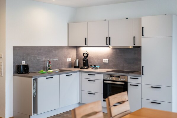 Een moderne keuken met witte kasten, een ingebouwde oven en een koffiezetapparaat.