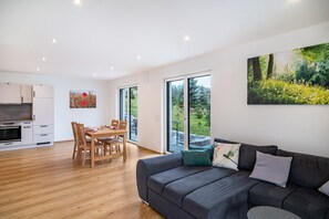 A modern living space with a dining area, kitchen, and large windows offering a view of greenery. - Holiday Apartment "Kiefer" with Private Terrace & Wi-Fi (Ravensburg)
