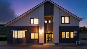 Une maison moderne à deux étages, dotée d’une entrée centrale, de grandes fenêtres et d’un climatiseur visible.