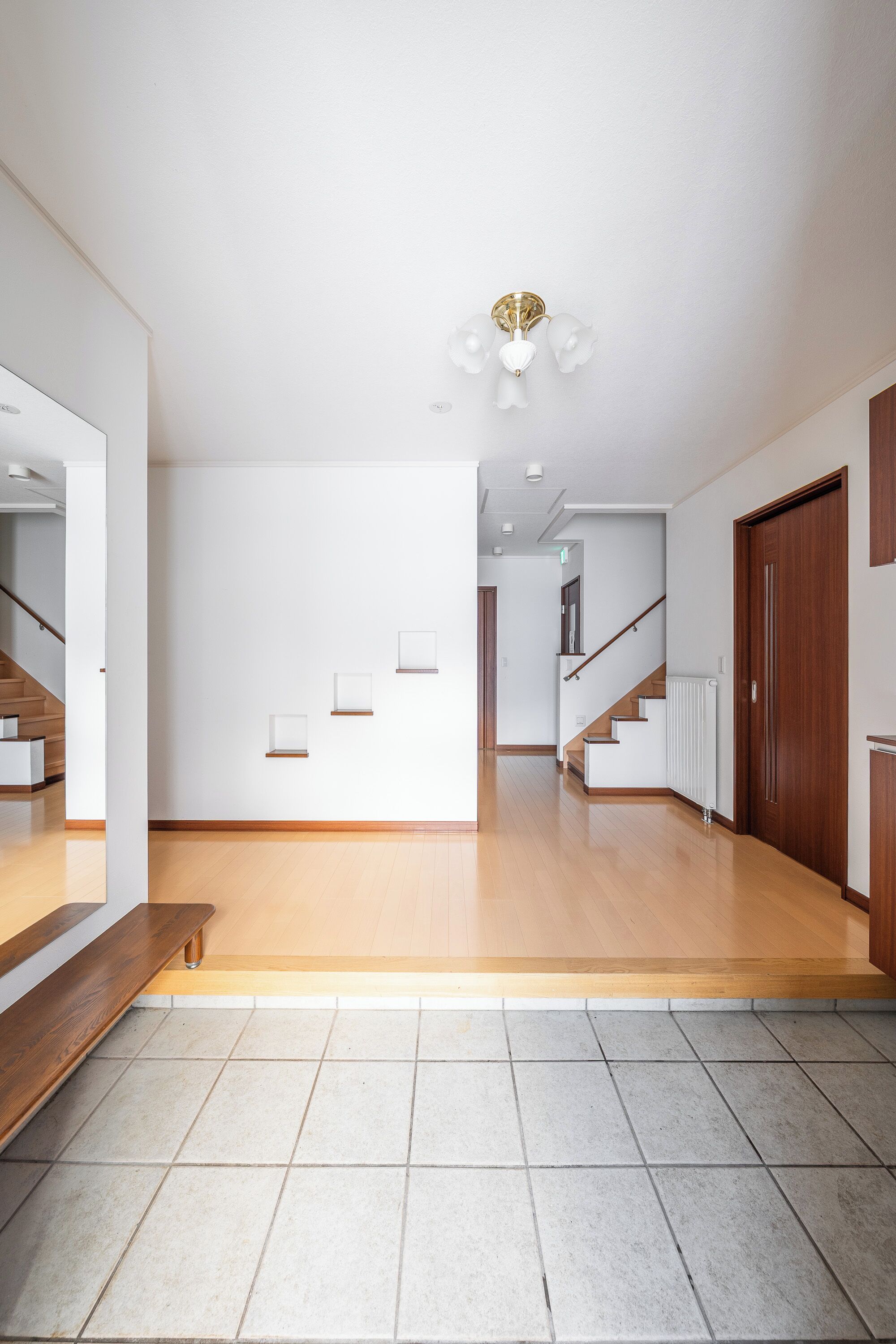 A spacious hallway with a wooden floor, white walls, and a staircase leading to another level.