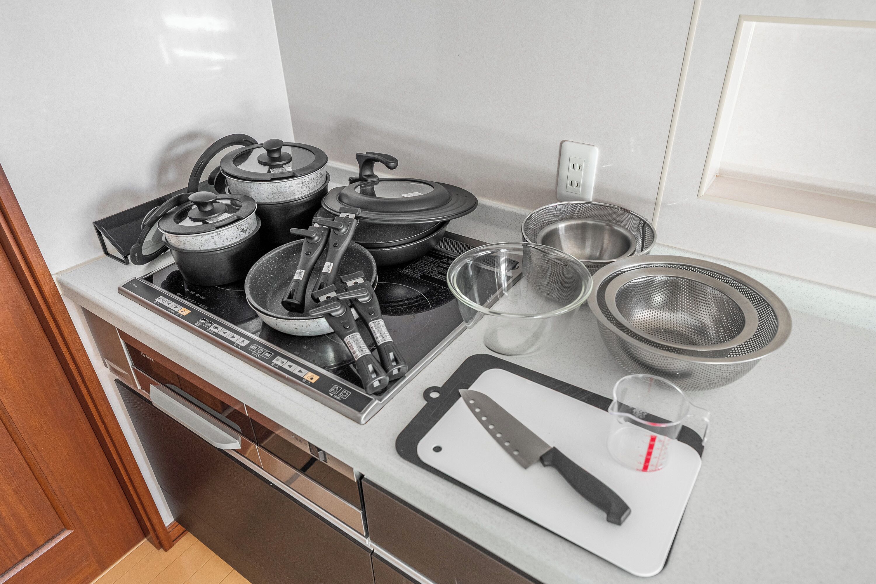 A kitchen with an induction cooktop, pots, pans, a cutting board, a knife, a measuring cup, and a colander.