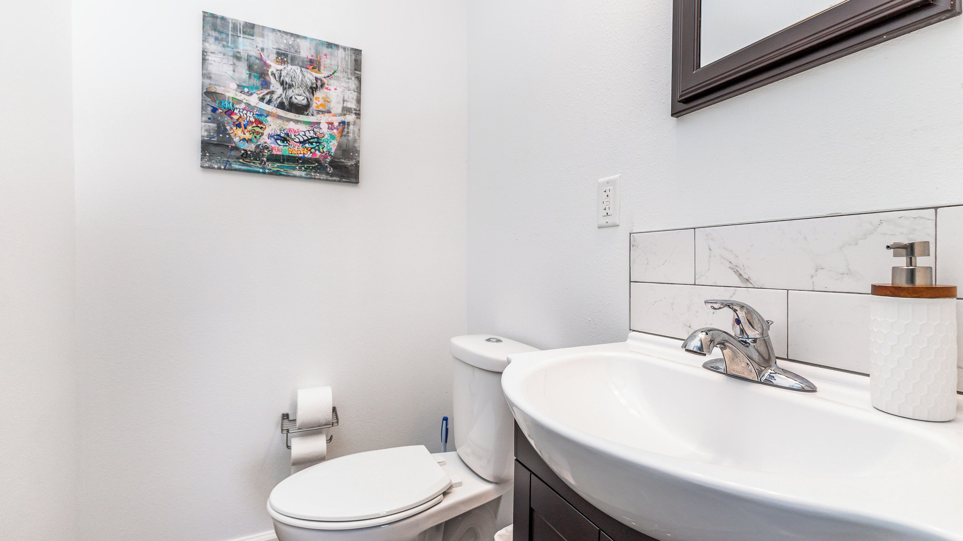 Een badkamer met een wit toilet, een wastafel met een marmeren spatwand en een schilderij aan de muur.