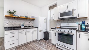 A modern kitchen with white cabinetry, a built-in oven, microwave, and a stainless steel range. There is a wooden shelf above the sink with dishes and a potted plant. - 1103#203 / Downtown Oasis: En-Suite Master (Dubuque)