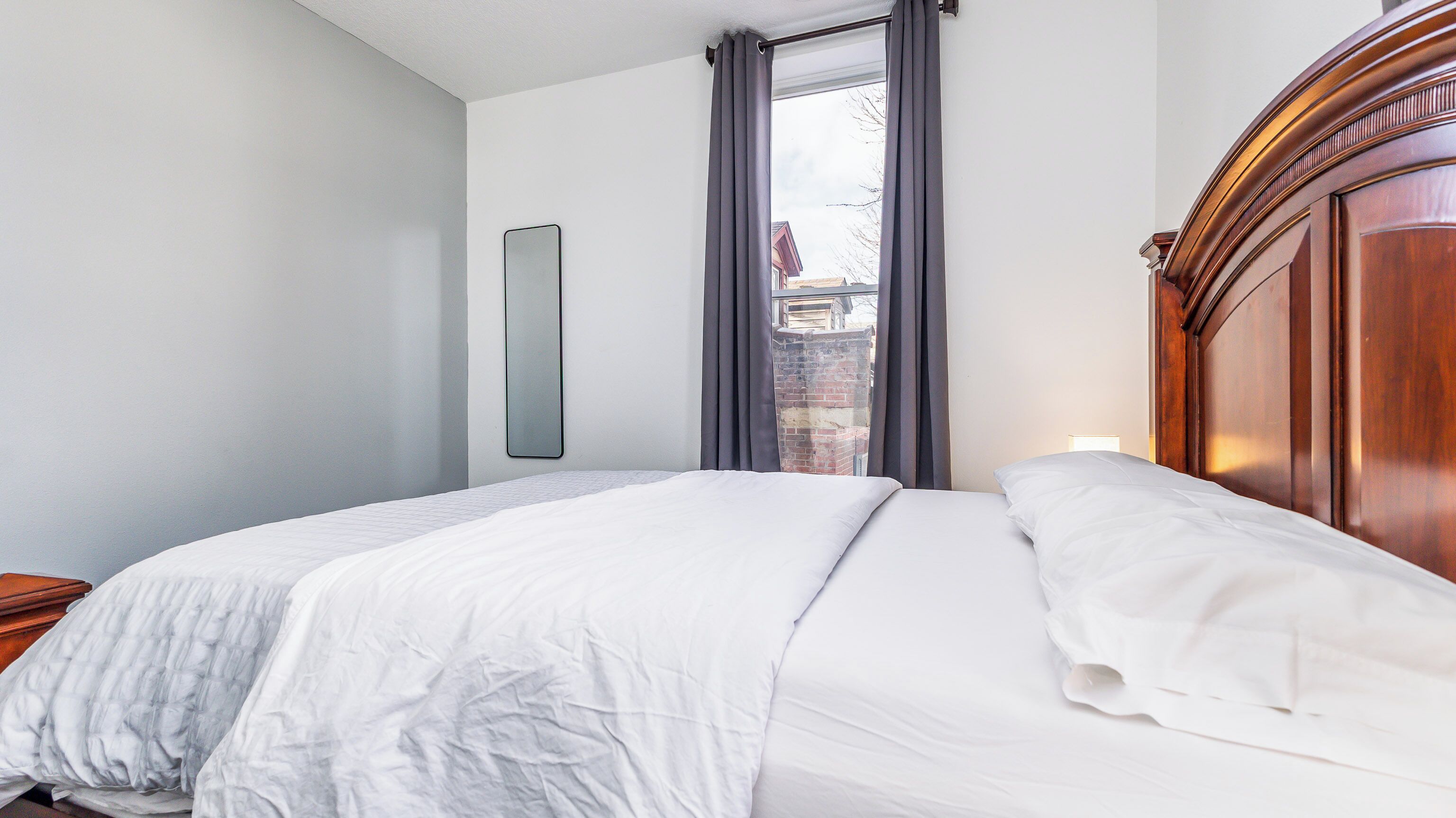 A bedroom with a large bed, a wooden headboard, a nightstand, and a window with curtains.