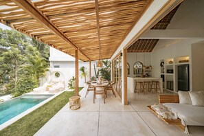 Een moderne buitenruimte met zwembad, houten pergola en een eethoek.