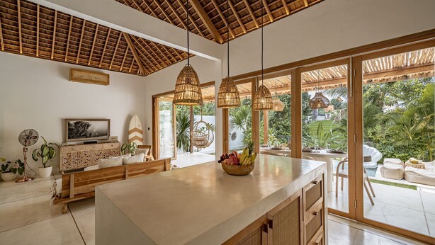 A spacious kitchen with a large island, wooden ceiling, and large windows offering a view of a lush garden. - Villa KerangSue (Canggu)